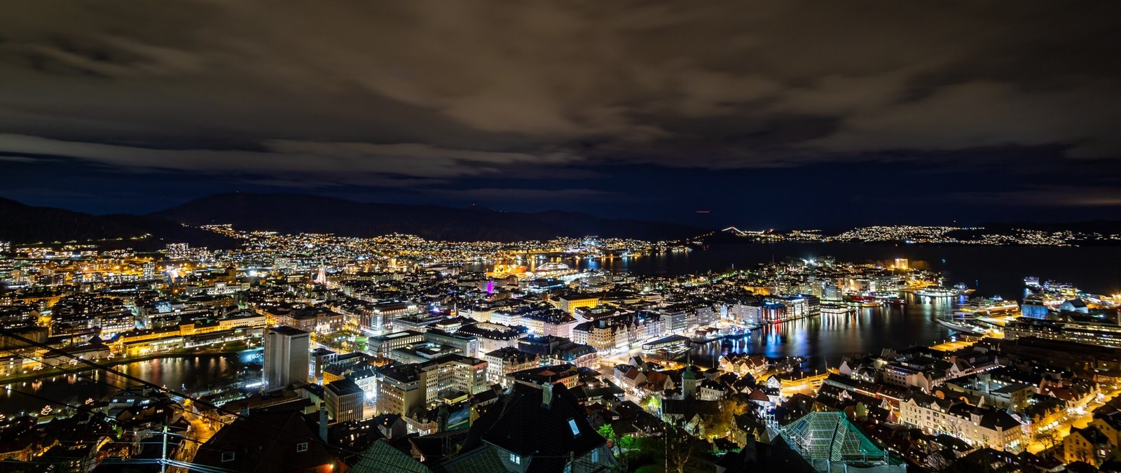 Panoramabilde av Bergen by om natten sett fra Fløyen, med lys over sentrum og havnen.
