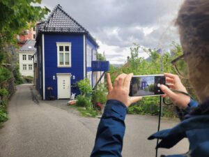 Person tar bilde av blått trehus i smal gate i Bergen