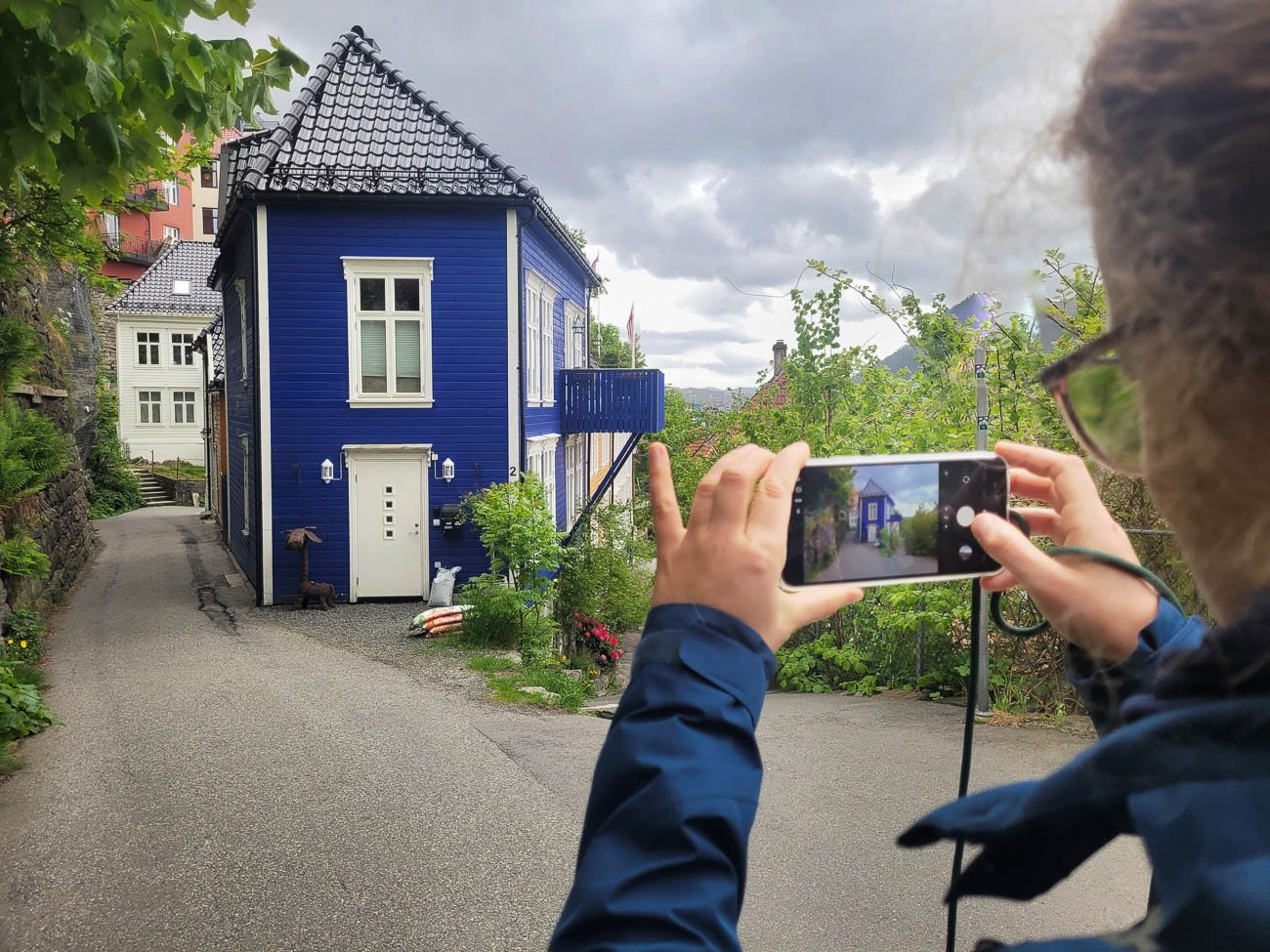 Person tar bilde av blått trehus i smal gate i Bergen