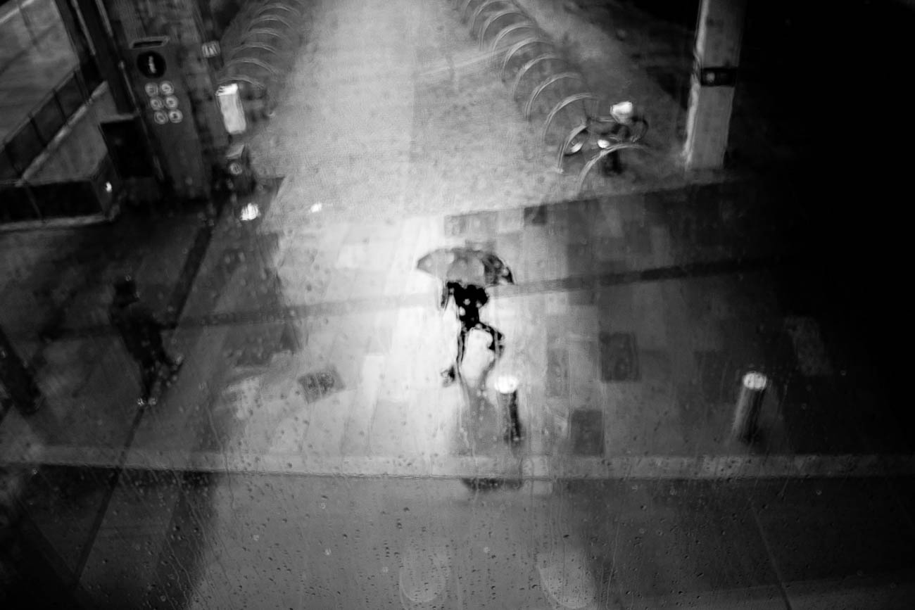 Person med paraply går gjennom regnvåt gate i Bergen sett ovenfra i svart-hvitt.