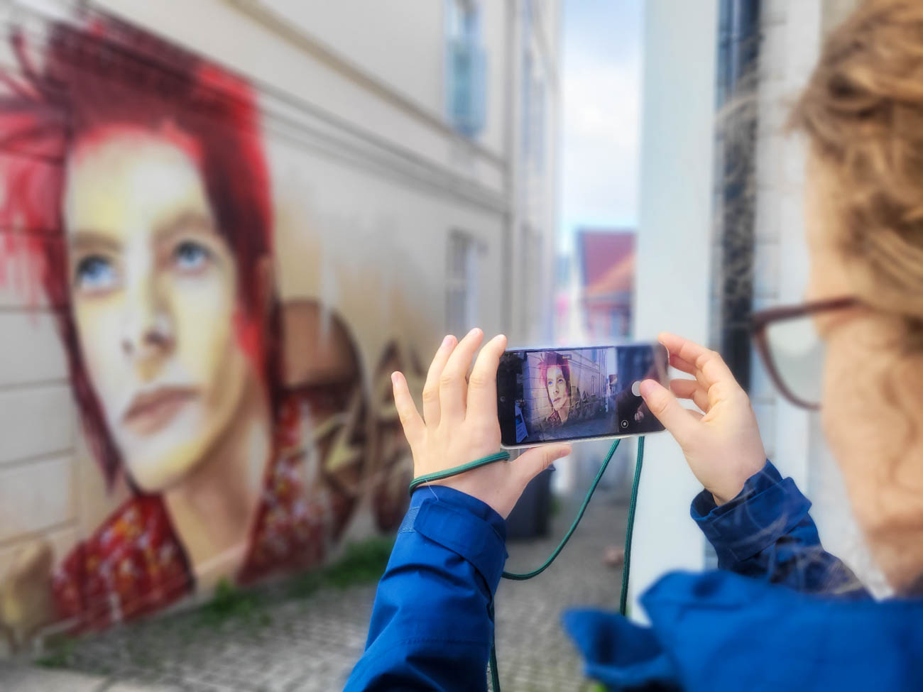 Person fotograferer gatekunst med mobiltelefon i et smalt byrom i Bergen.